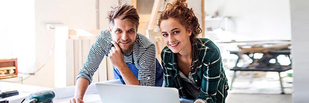 Seguro de Responsabilidad Civil Autonomos - Pareja joven de autonomos sonriendo con un portatil mientras trabajan en una carpinteria Seguro de Responsabilidad Civil Autonomos - Pareja joven de autonomos sonriendo con un portatil mientras trabajan en una carpinteria